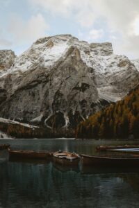 Wooden boats on tranquil Lago di Braies with snow-kissed Dolomites and autumn foliage.